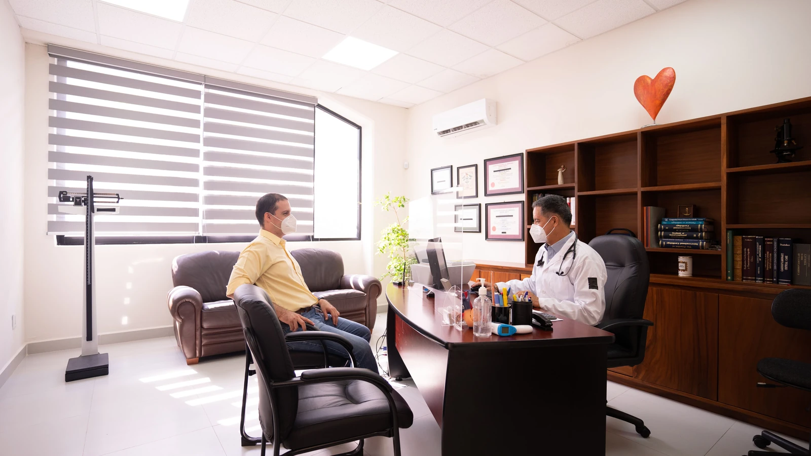Un paziente consulta con un medico mascherato in un ufficio moderno e ben illuminato. Misure di sicurezza attuate.