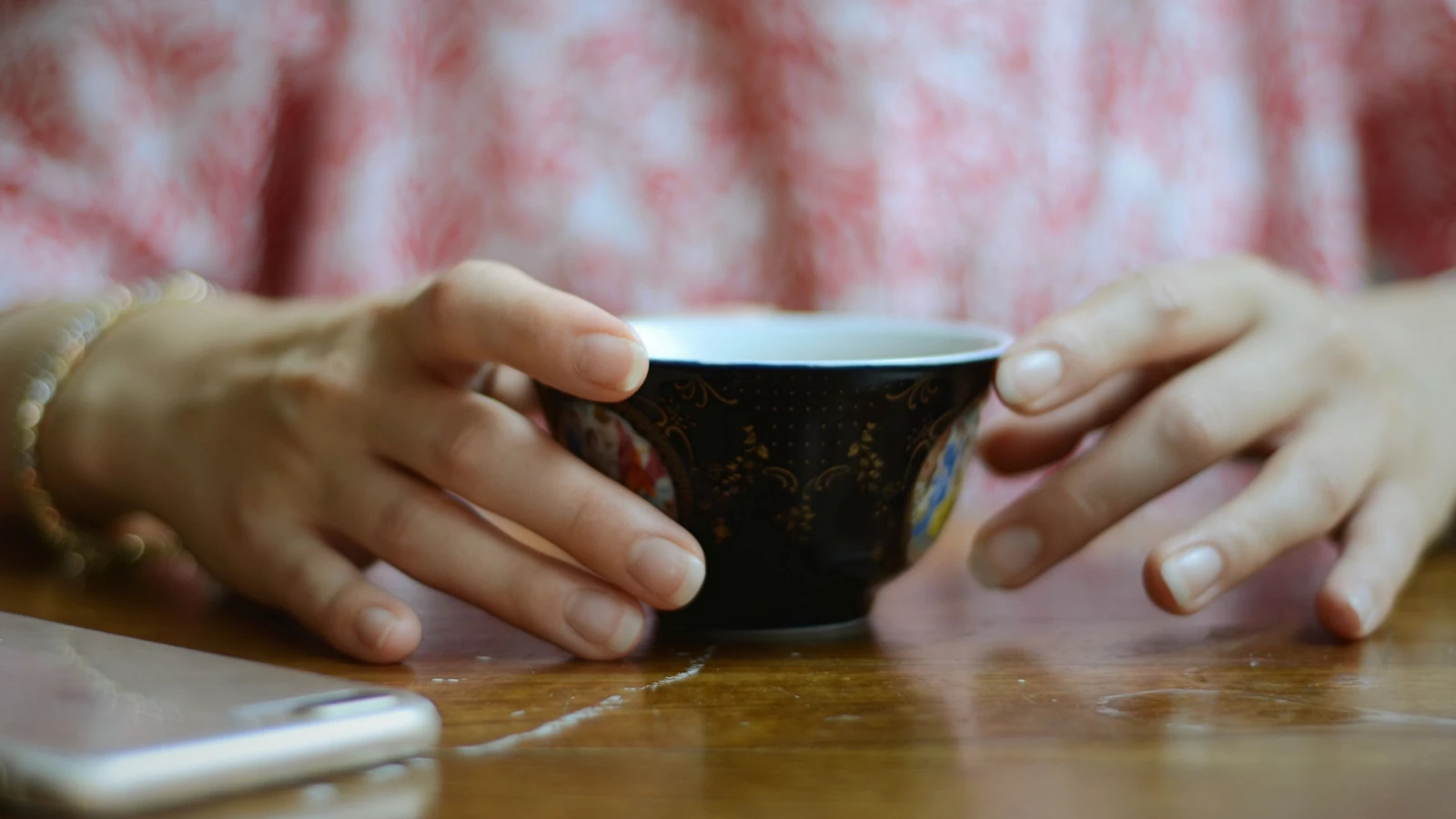 Mani che tengono una tazza decorativa su un tavolo di legno, riflettendo il relax del mattino all'interno.