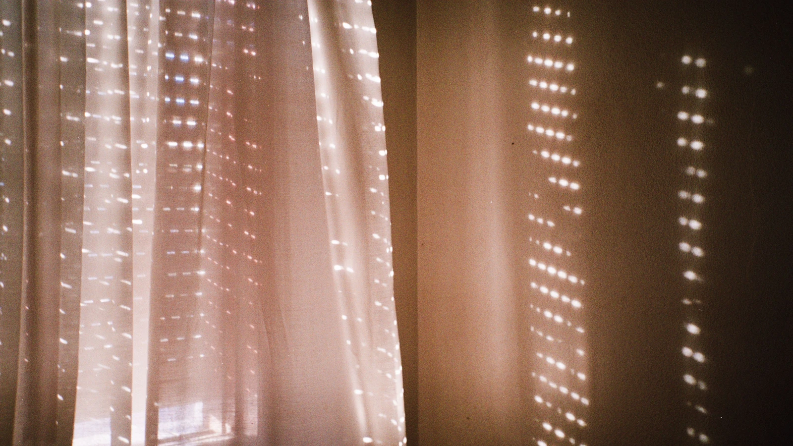 La luce del sole filtra attraverso le persiane creando un sereno motivo di ombre su una tenda bianca all'interno.