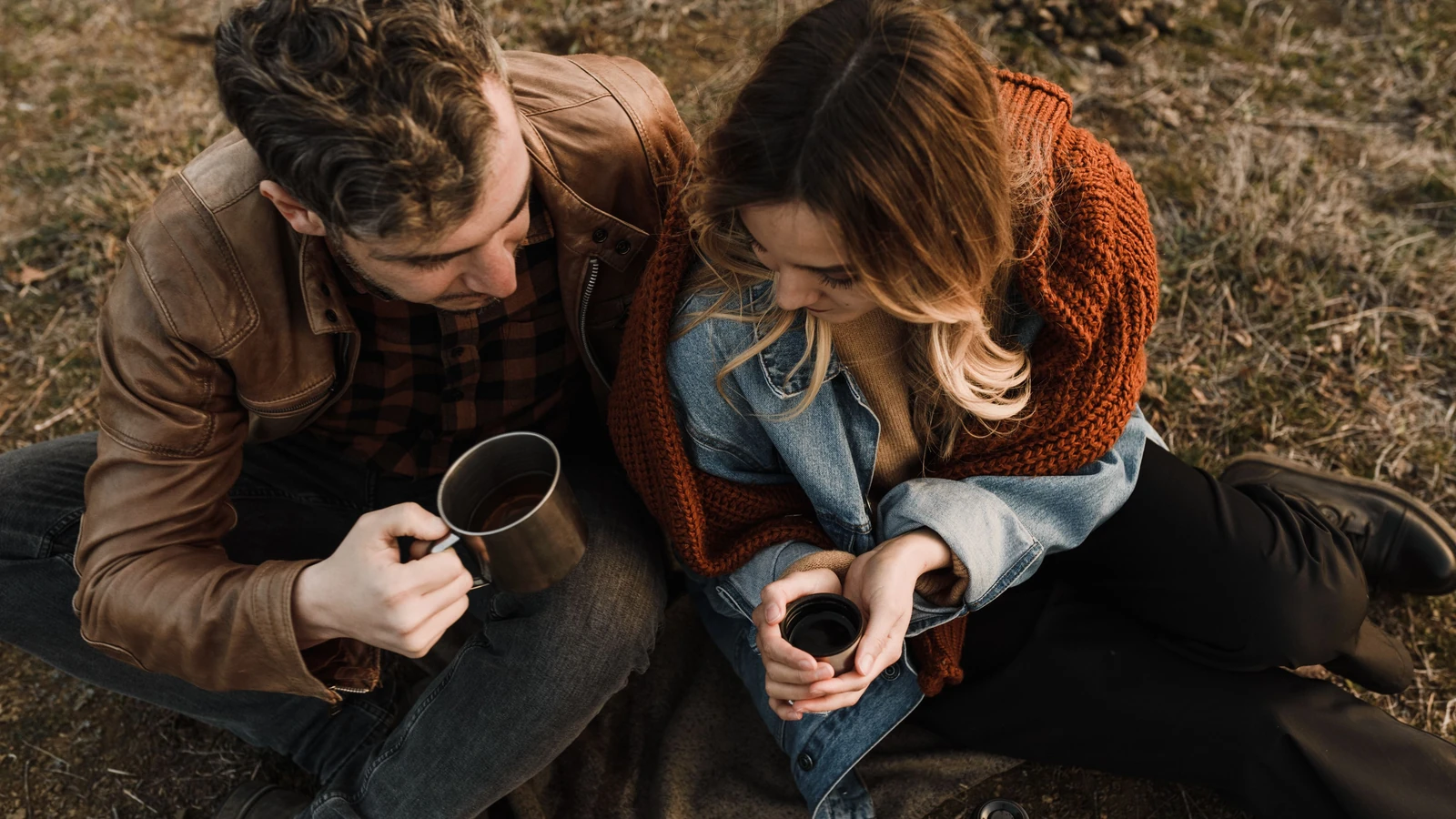 Una coppia seduta all'aperto con tazze, che gode di una bevanda calda e condivide un momento romantico.