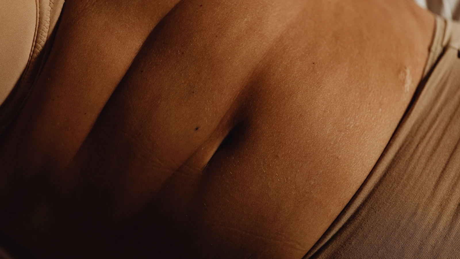 Primo piano dettagliato dell'addome di una donna e dell'ombelico in intimo beige, mostrando la texture della pelle.