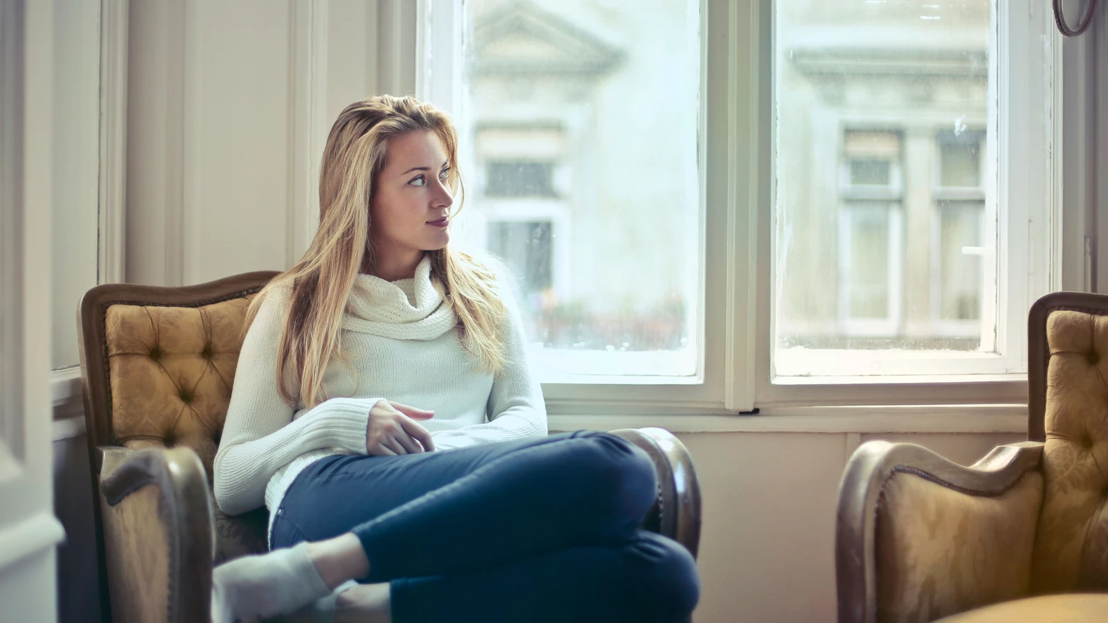 Un momento sereno di una donna in una stanza accogliente, mentre si gode il tempo libero vicino alla finestra.
