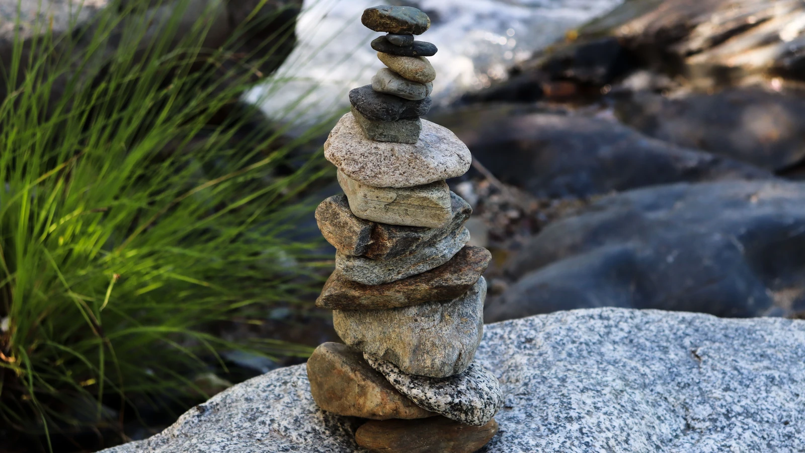 Una torre di pietre accuratamente impilate su una roccia accanto a un ruscello, che simboleggia armonia e equilibrio.