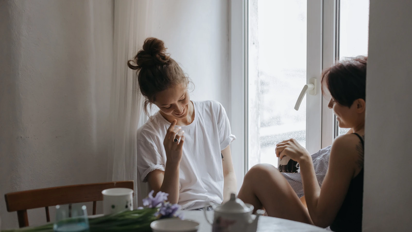 Due donne che godono di una conversazione rilassata vicino a una finestra con un'atmosfera accogliente.