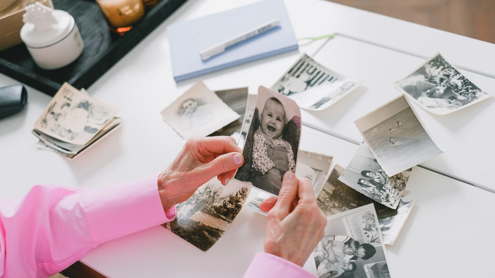 Una persona con una camicia rosa che organizza vecchie foto di famiglia in bianco e nero su un tavolo.