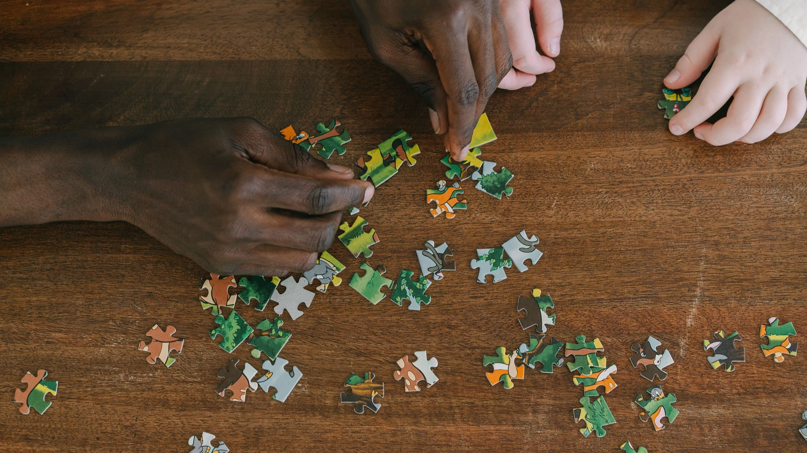 Due mani collaborano per risolvere un puzzle su una superficie di legno, enfatizzando il lavoro di squadra.