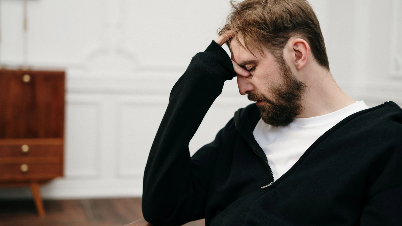 Un uomo siede pensieroso con la mano sul viso, catturando un momento di introspezione e stress.
