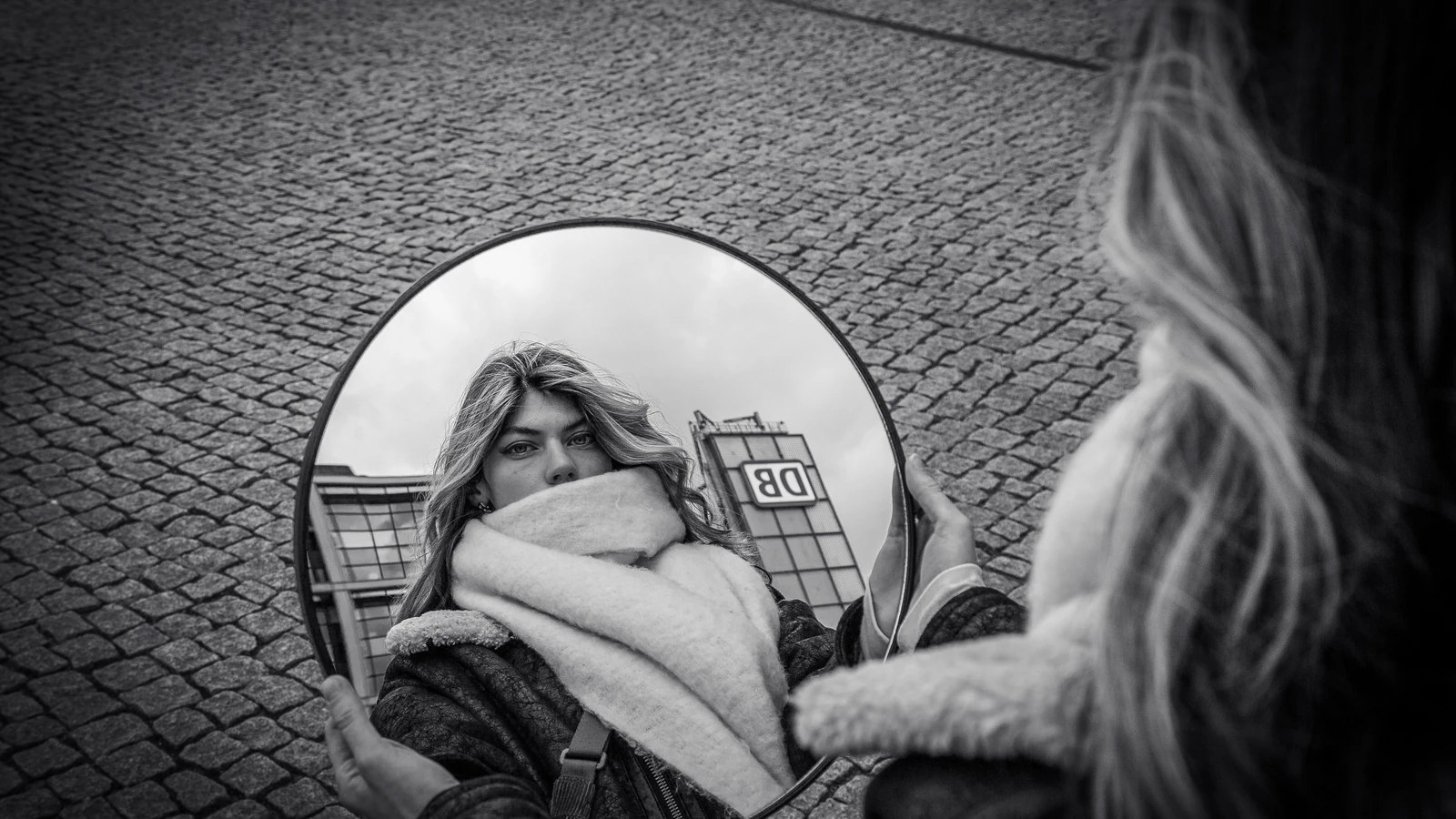 Foto in bianco e nero di una donna riflessa in uno specchio per le strade di Berlino.