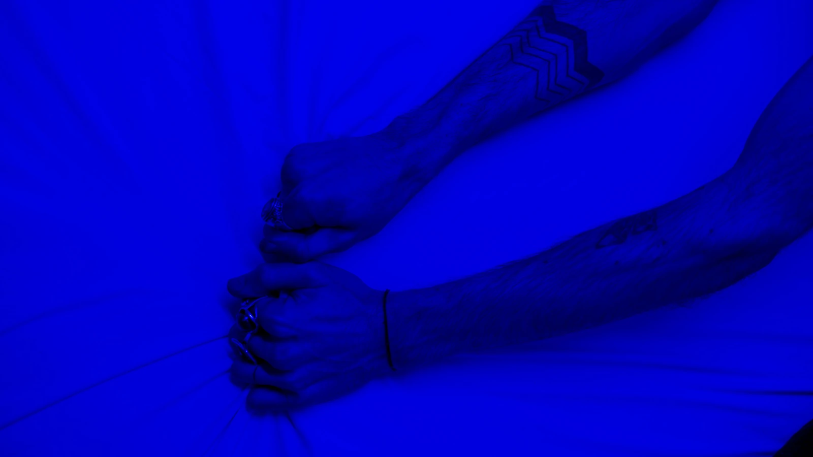 Primo piano di braccia tatuate che tirano il tessuto sotto un'intensa luce blu, simboleggiando stress o frustrazione.