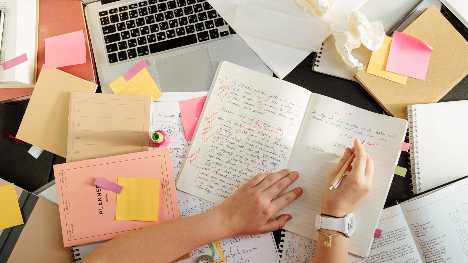 Scatto dall'alto di una persona che organizza appunti e materiali di studio su una scrivania ingombra con un laptop. — cottonbro studio – Pexels
