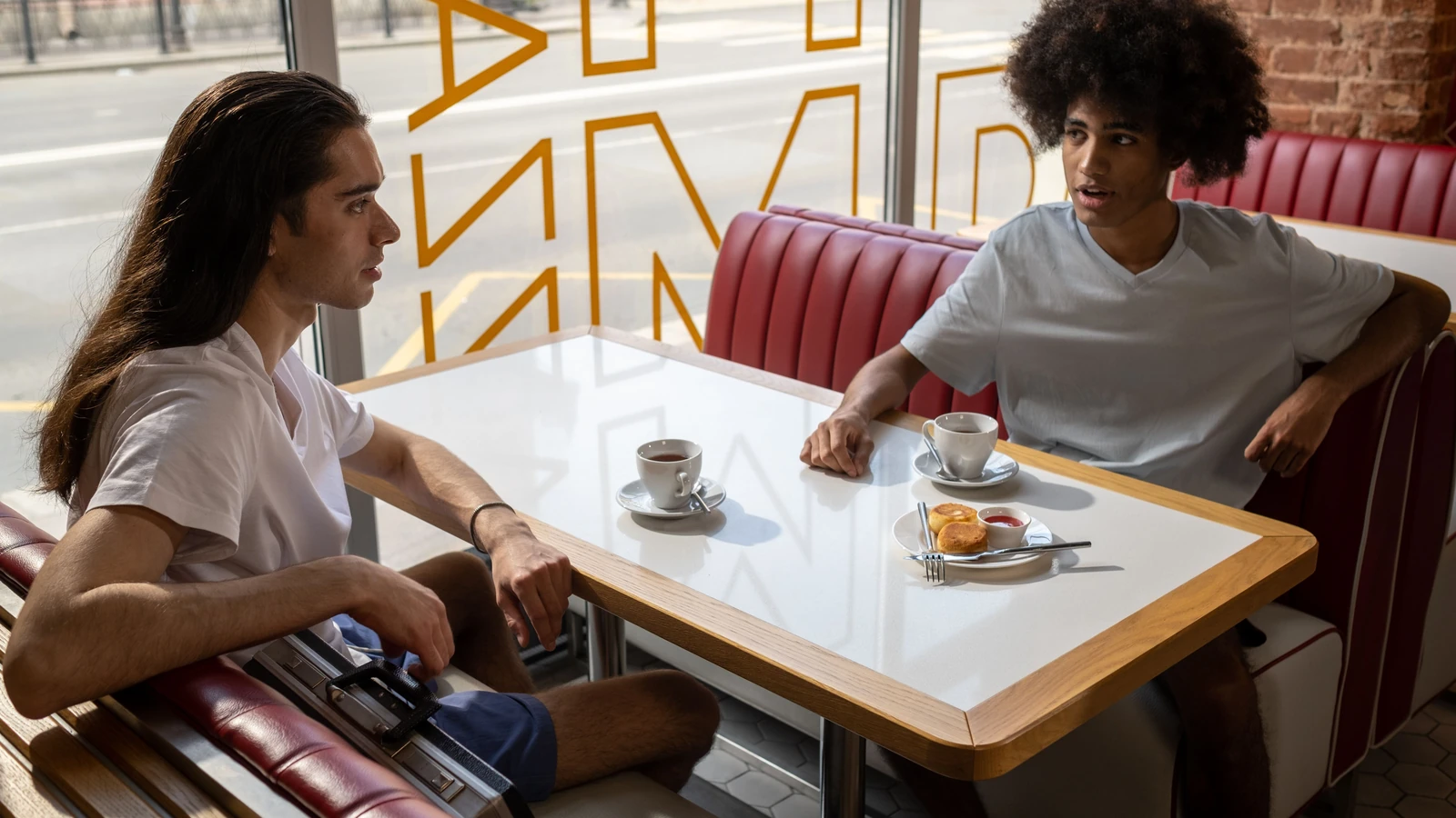Due amici conversano sorseggiando caffè e pasticcini in un ambiente da caffè elegante.