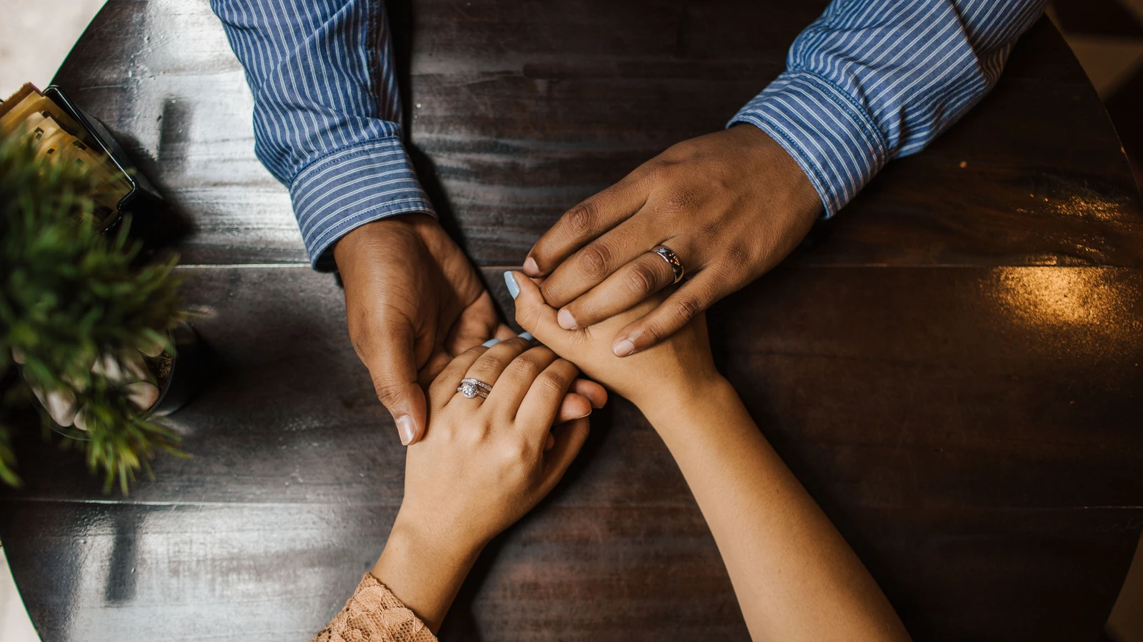 Una coppia che si tiene per mano su un tavolo di legno, esprimendo amore e connessione. — Luis Quintero – Pexels