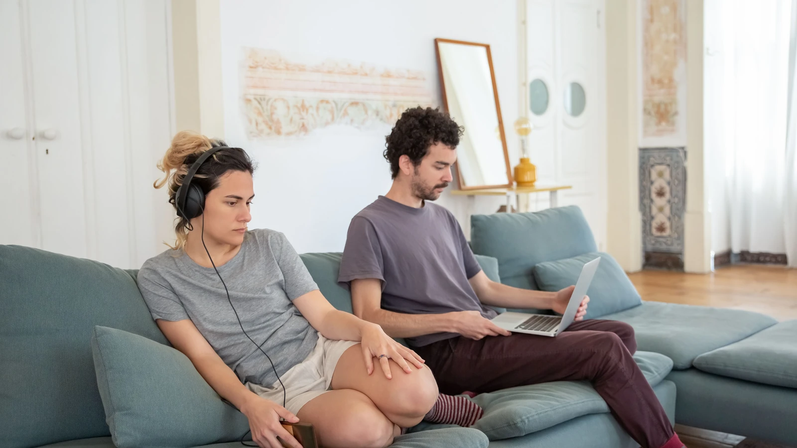 Una coppia che si rilassa su un divano con cuffie e laptop, creando un'atmosfera accogliente in casa.