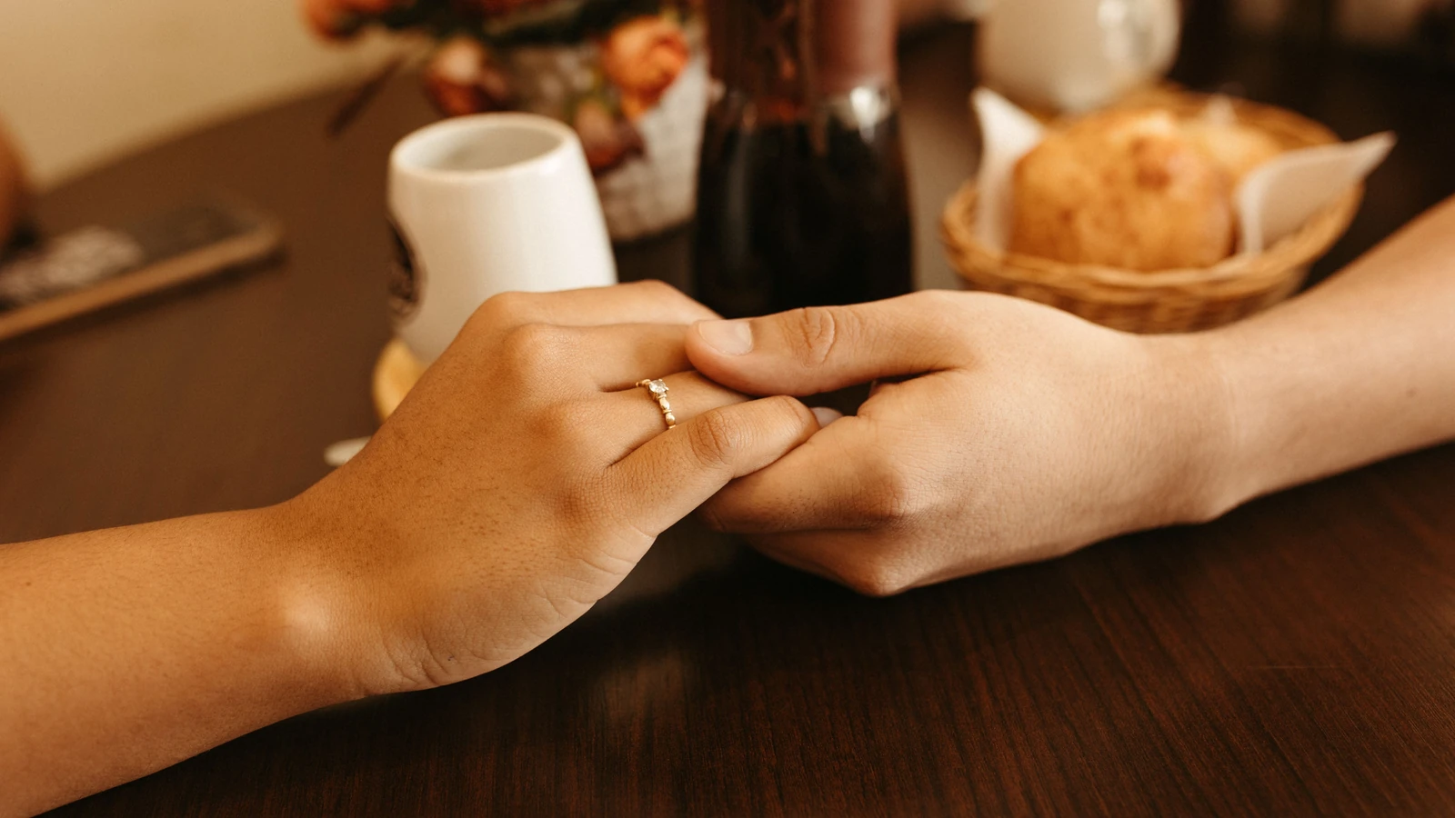 Primo piano di una coppia romantica che si tiene per mano a un tavolo del caffè, evidenziando un anello di fidanzamento.