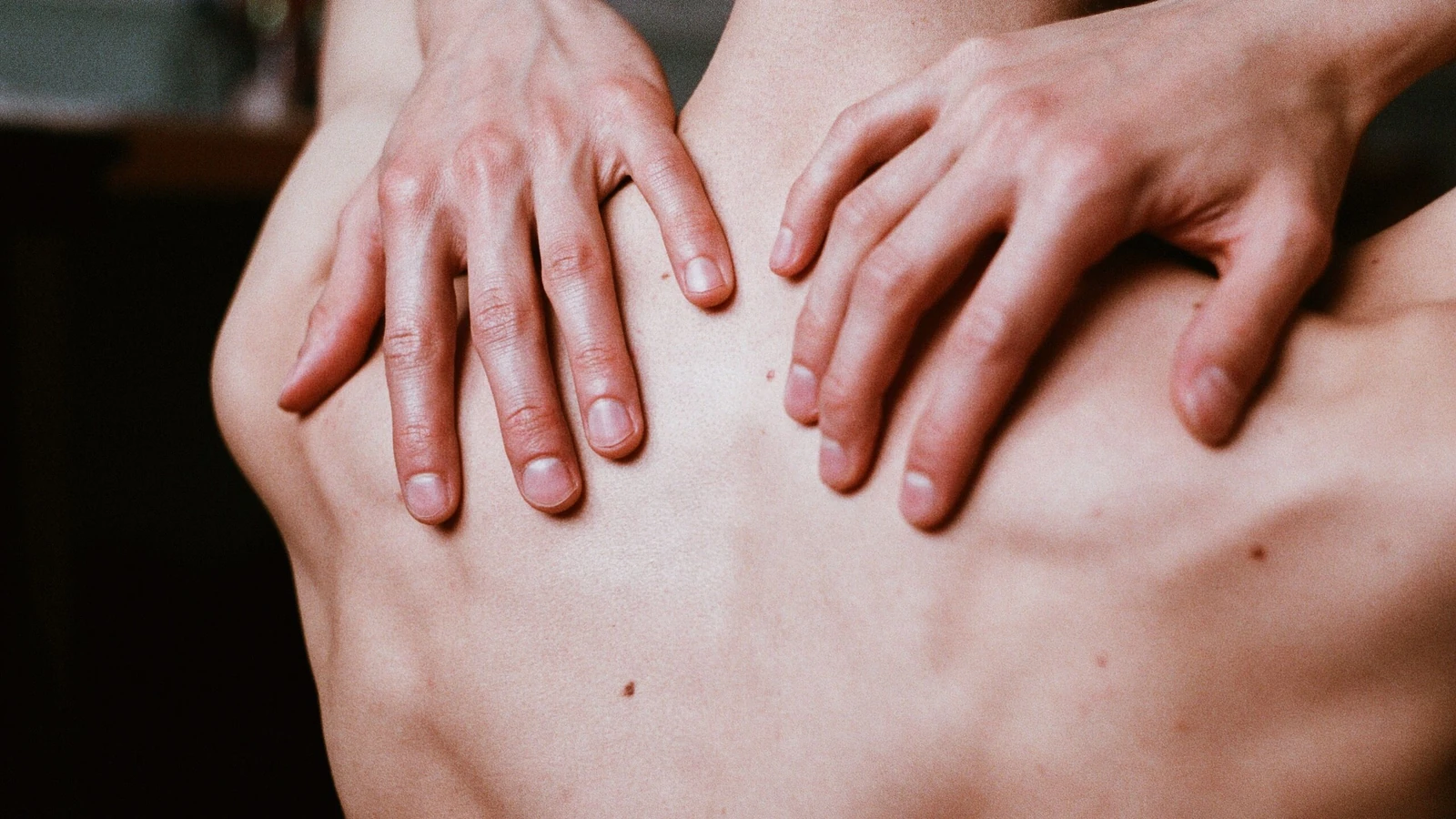 Scatto estetico in primo piano delle mani di un uomo posizionate sulla sua schiena nuda, creando un'immagine calmante e contemplativa.