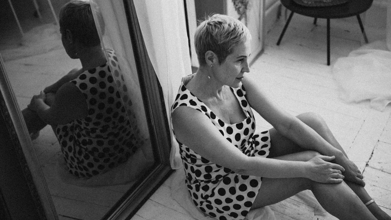 Foto in bianco e nero di una donna riflessa in uno specchio, che indossa un abito a pois.