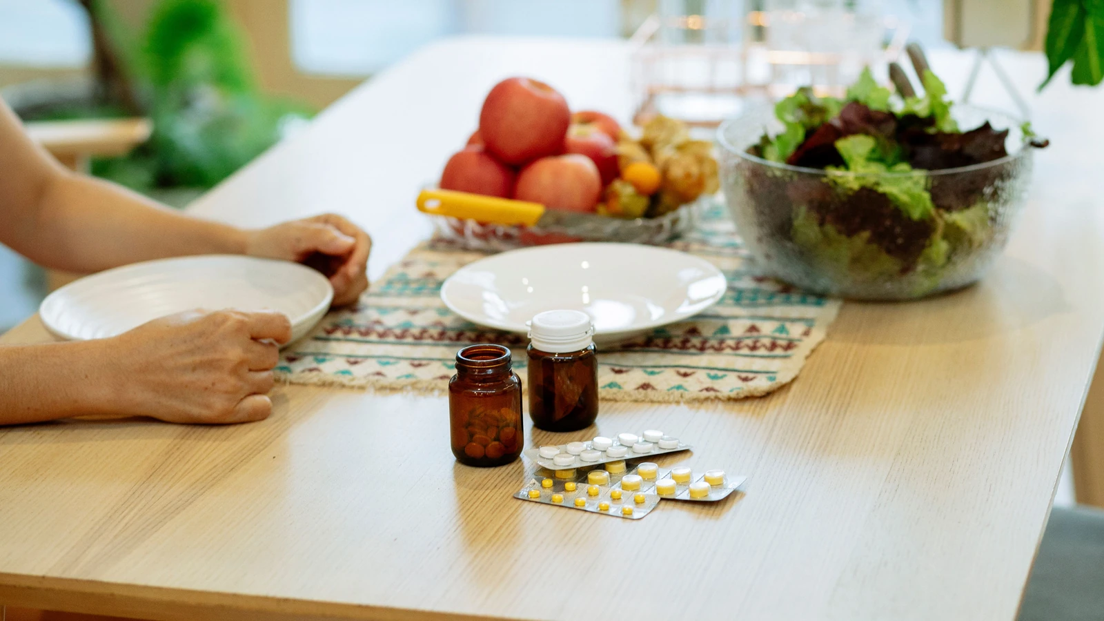 Un tavolo impostato con insalata, frutta e farmaci, che promuove uno stile di vita sano al chiuso. — Michelle Leman – Pexels