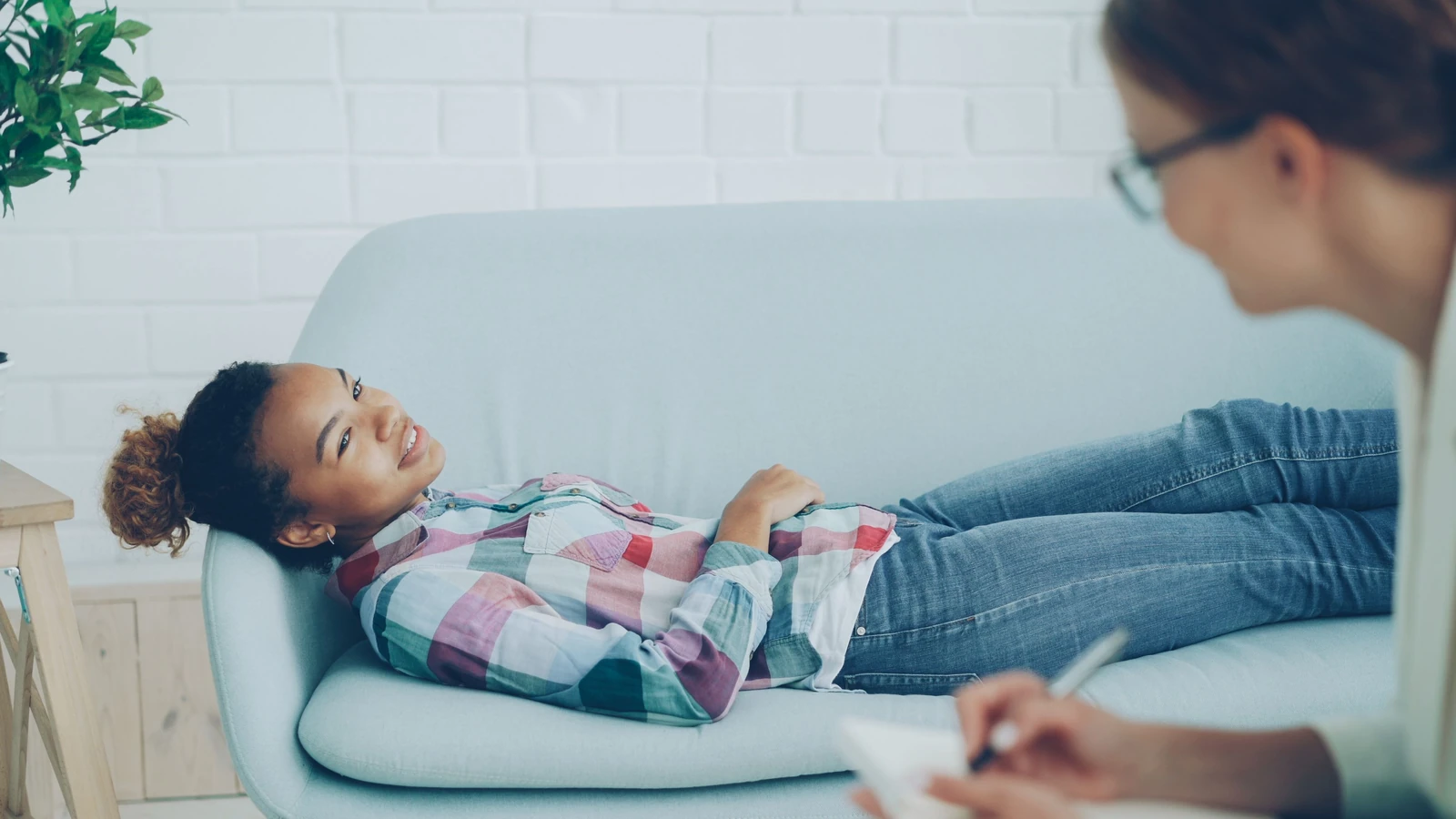 Una donna in terapia, sorridente mentre è sdraiata su un divano, con un consulente che prende appunti.