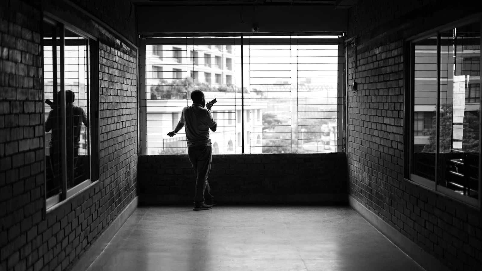 Silhouette di una persona vicino a una finestra in un corridoio moderno con vista urbana, foto in bianco e nero.