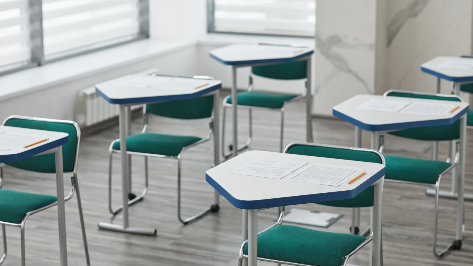 Un'aula vuota con banchi disposti, fogli d'esame e matite pronte per gli studenti.