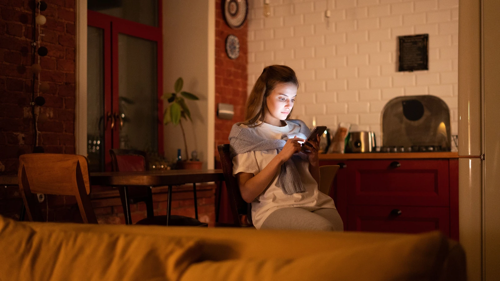 Una donna che usa il suo smartphone in un ambiente domestico accogliente durante la sera.