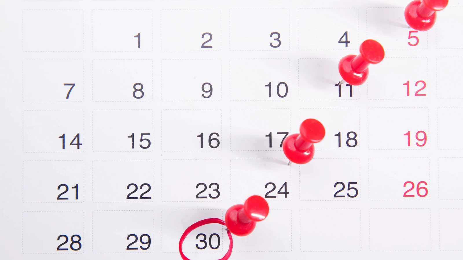 Primo piano di un calendario con puntine rosse che evidenziano date importanti e scadenze.