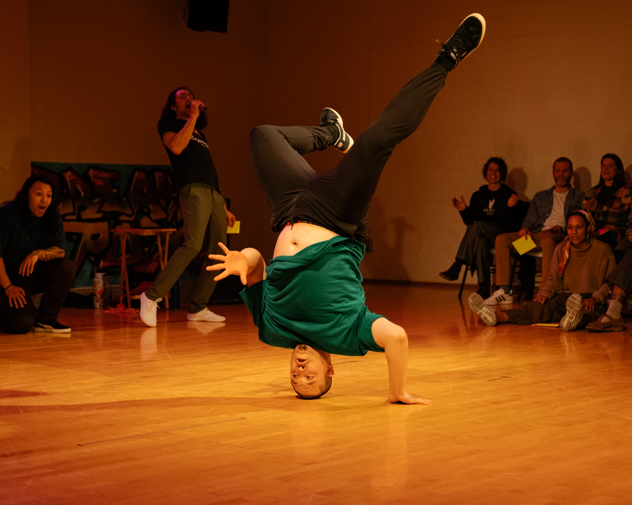 Doe Rock - aka Spencer - is frozen in a headstand with one arm touch the ground and the other waving at another dancer.