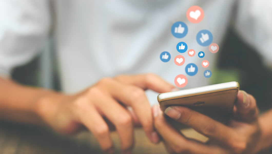 Person holding mobile phone with social media like buttons coming from it