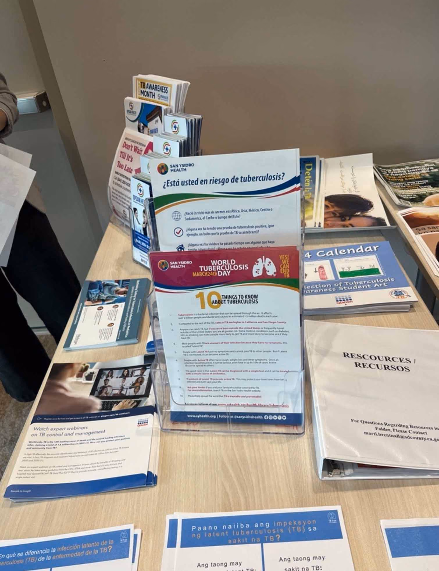Table display with tuberculosis awareness brochures and resources in multiple languages including English and Spanish.