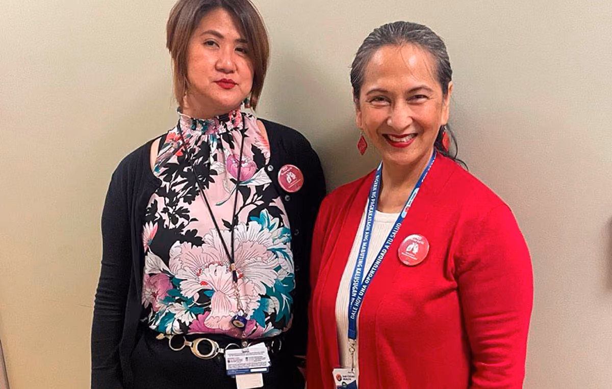 Two women smiling and standing side by side wearing ID badges and red buttons.