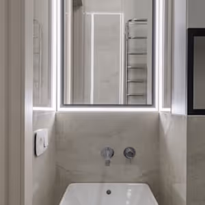 Modern bathroom sink with wall-mounted faucet, large mirror, and towel rack reflected in mirror.