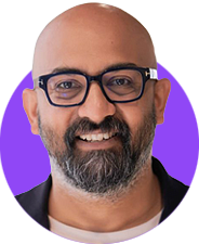 A headshot of a smiling bald man with a grey and black short beard and dark glasses edited within a simple circle graphic that has a bright purple background.