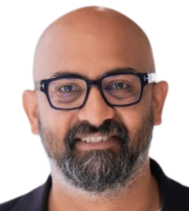 A headshot of a smiling bald man with a grey and black short beard and dark glasses edited within a simple circle graphic that has a bright purple background.