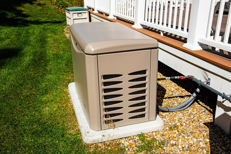 Outdoor standby generator installed next to a house, positioned on a concrete pad.