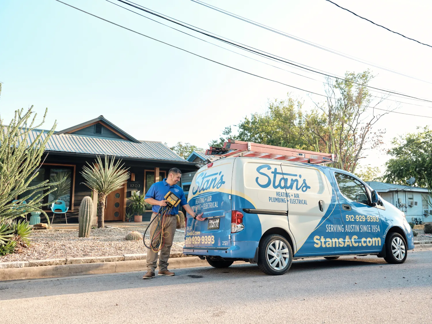 A technician from Stan's Heating, Air, Plumbing, and Electrical is standing beside a company van parked in front of a modern house. He is holding a diagnostic tool and looking at the van.

