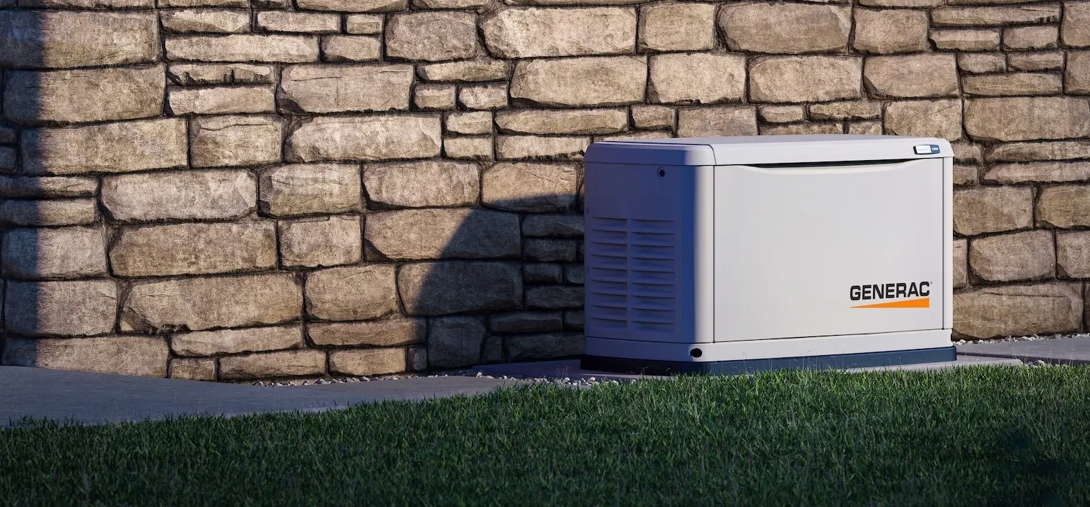 A Generac generator is positioned next to a stone wall outside a house. The area around the generator is neatly maintained, and the setup is professionally installed.