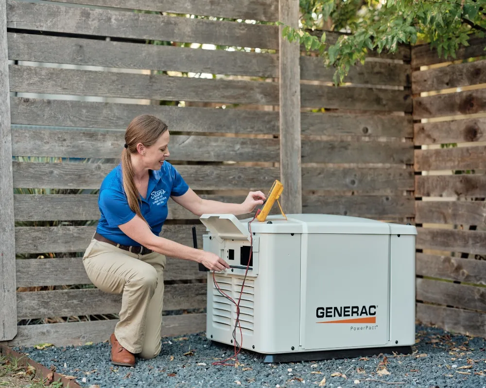 female technician from Stan's is adjusting the settings on a Generac generator. She is kneeling on gravel and using a multimeter to test the connections.