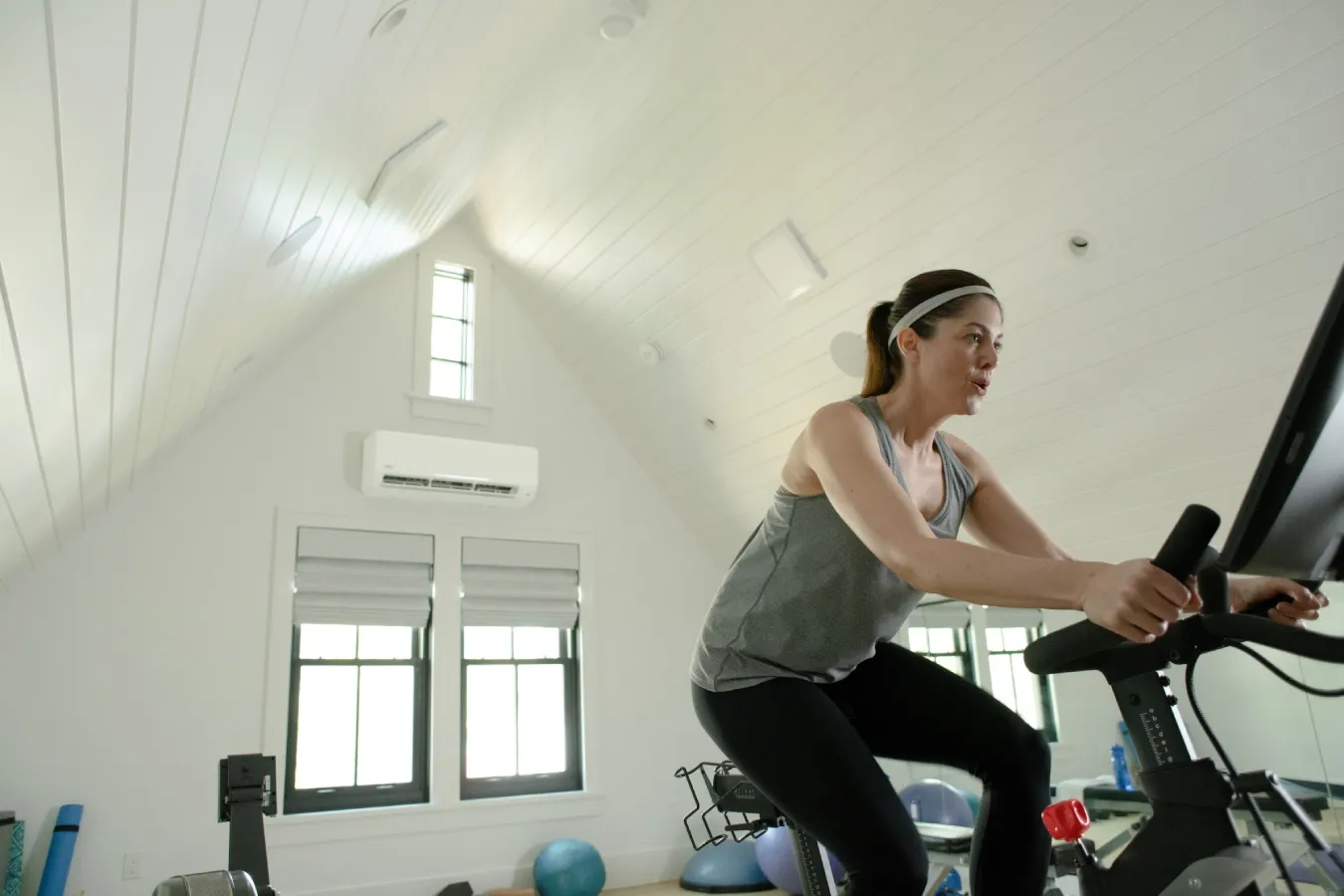 Person exercising on a stationary bike in a bright room with slanted ceiling.