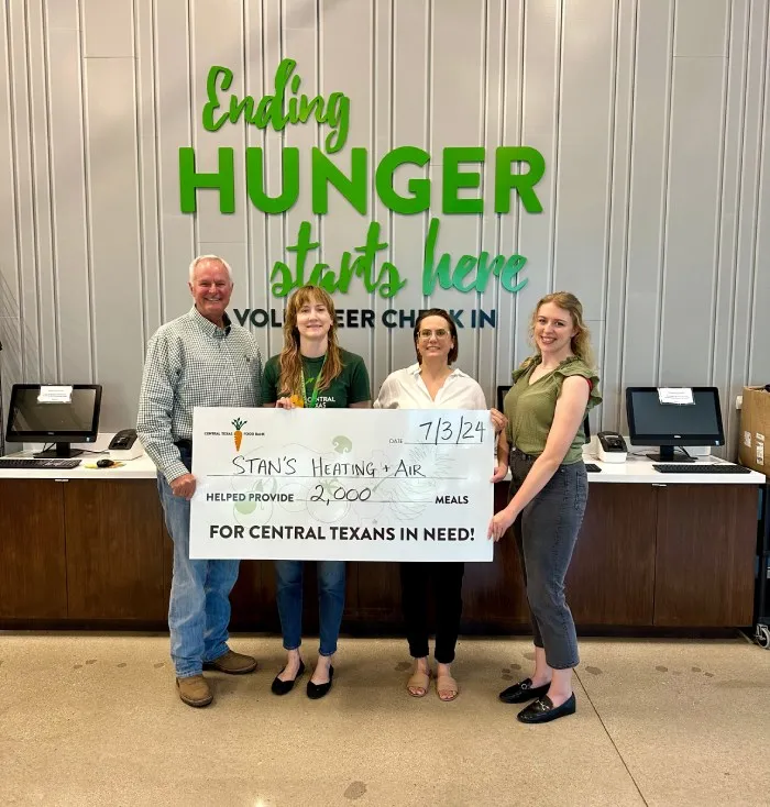 Four people standing together holding a large donation check in a room with a sign that says "Ending Hunger Starts Here."