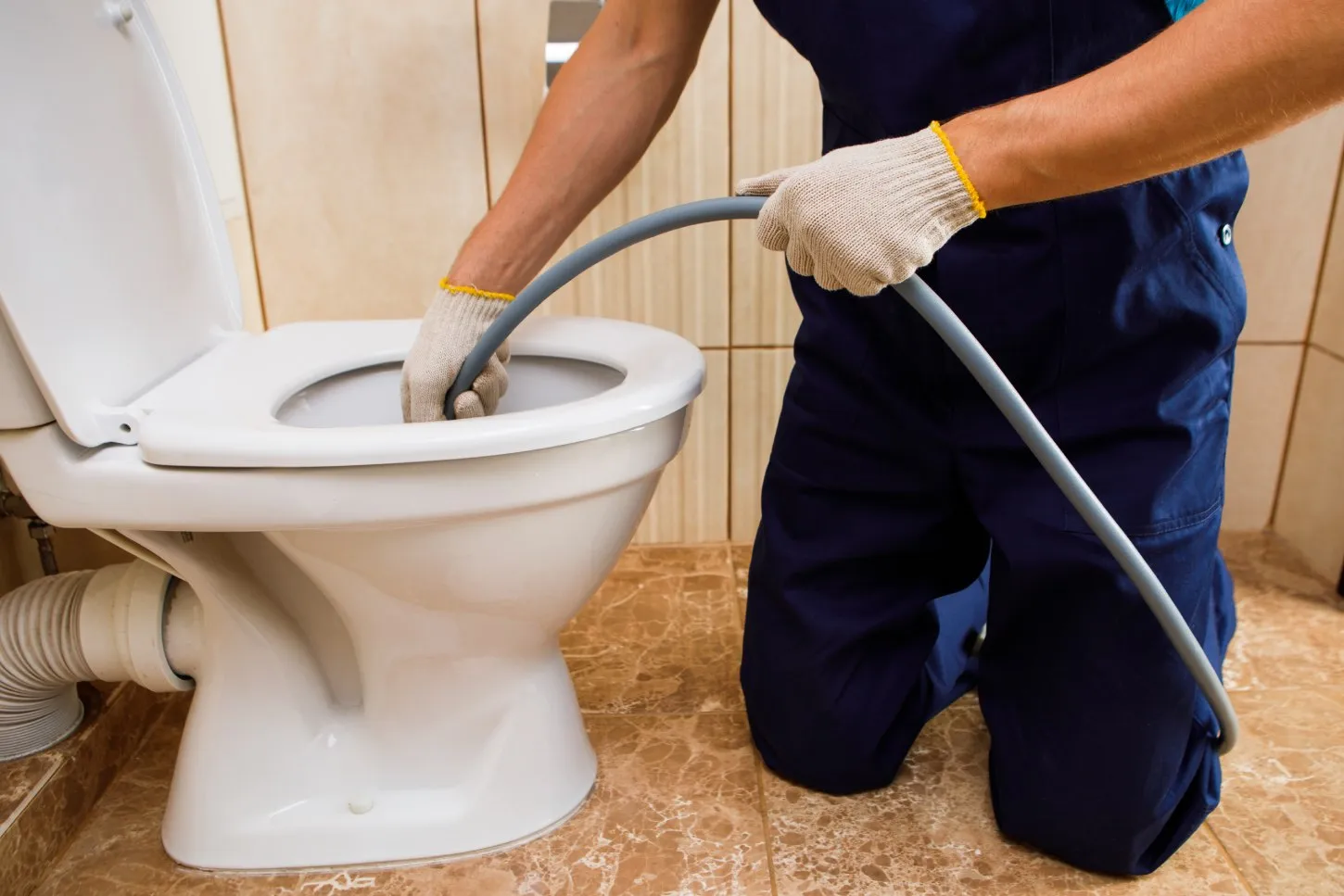 Person kneeling and using a plumbing snake to unclog a toilet.