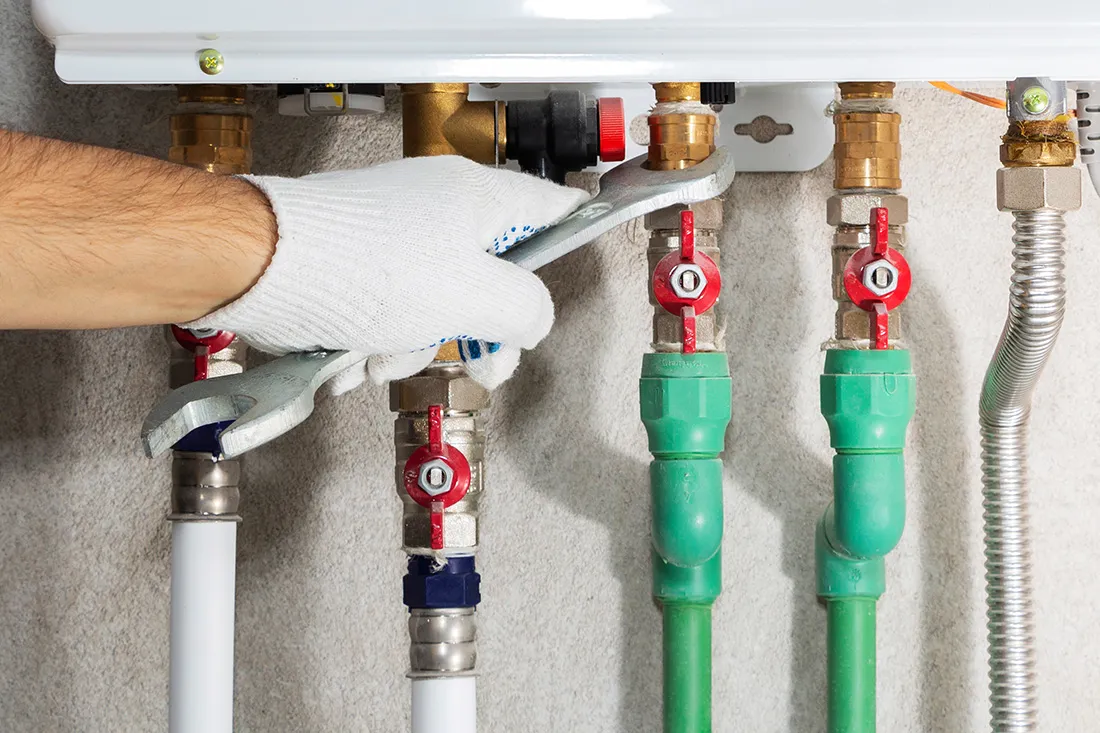 A person wearing a glove uses a wrench to adjust a valve on a series of connected pipes.