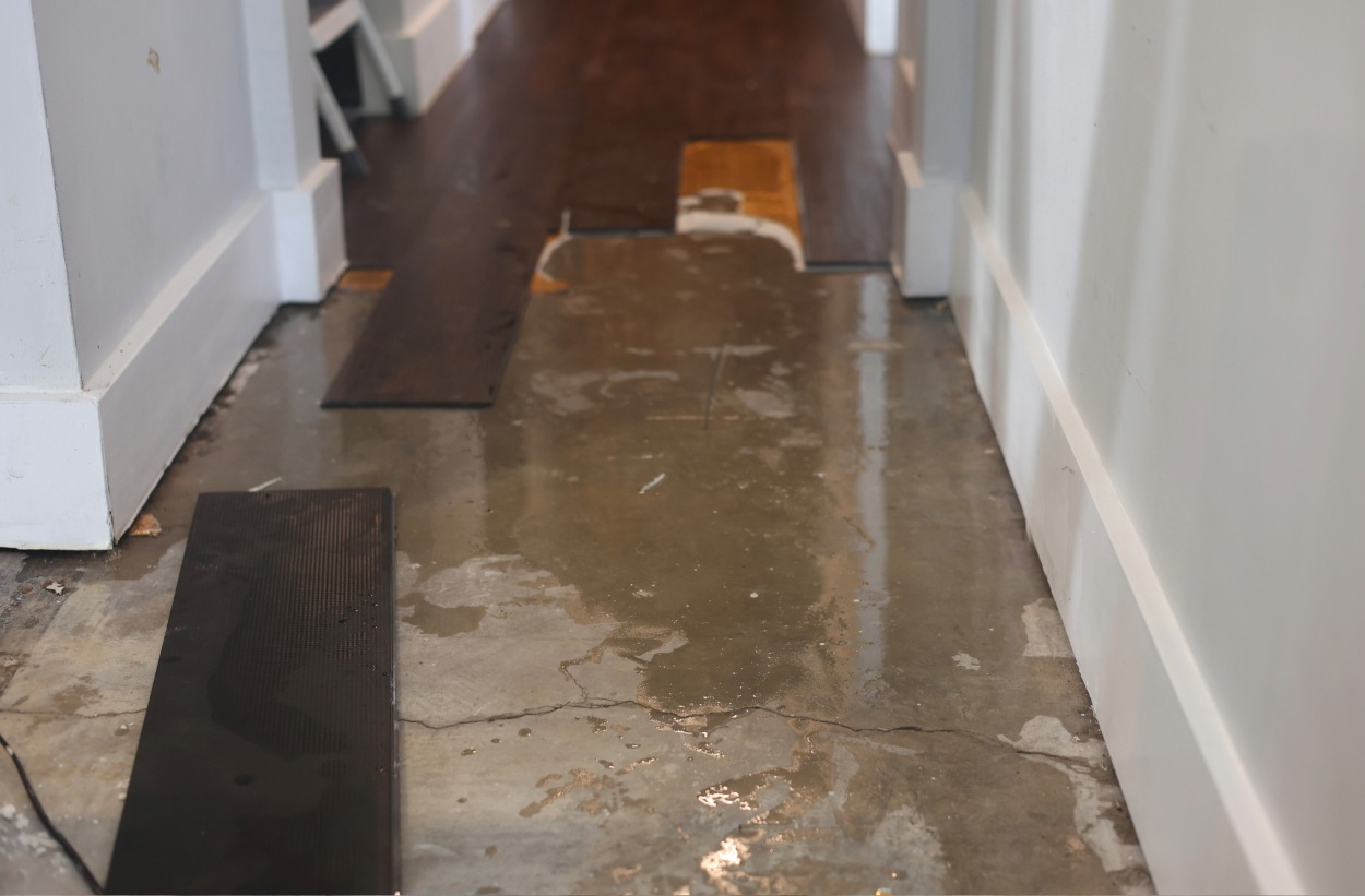 Partially installed dark wood flooring on a concrete subfloor in a narrow hallway with white baseboards.
