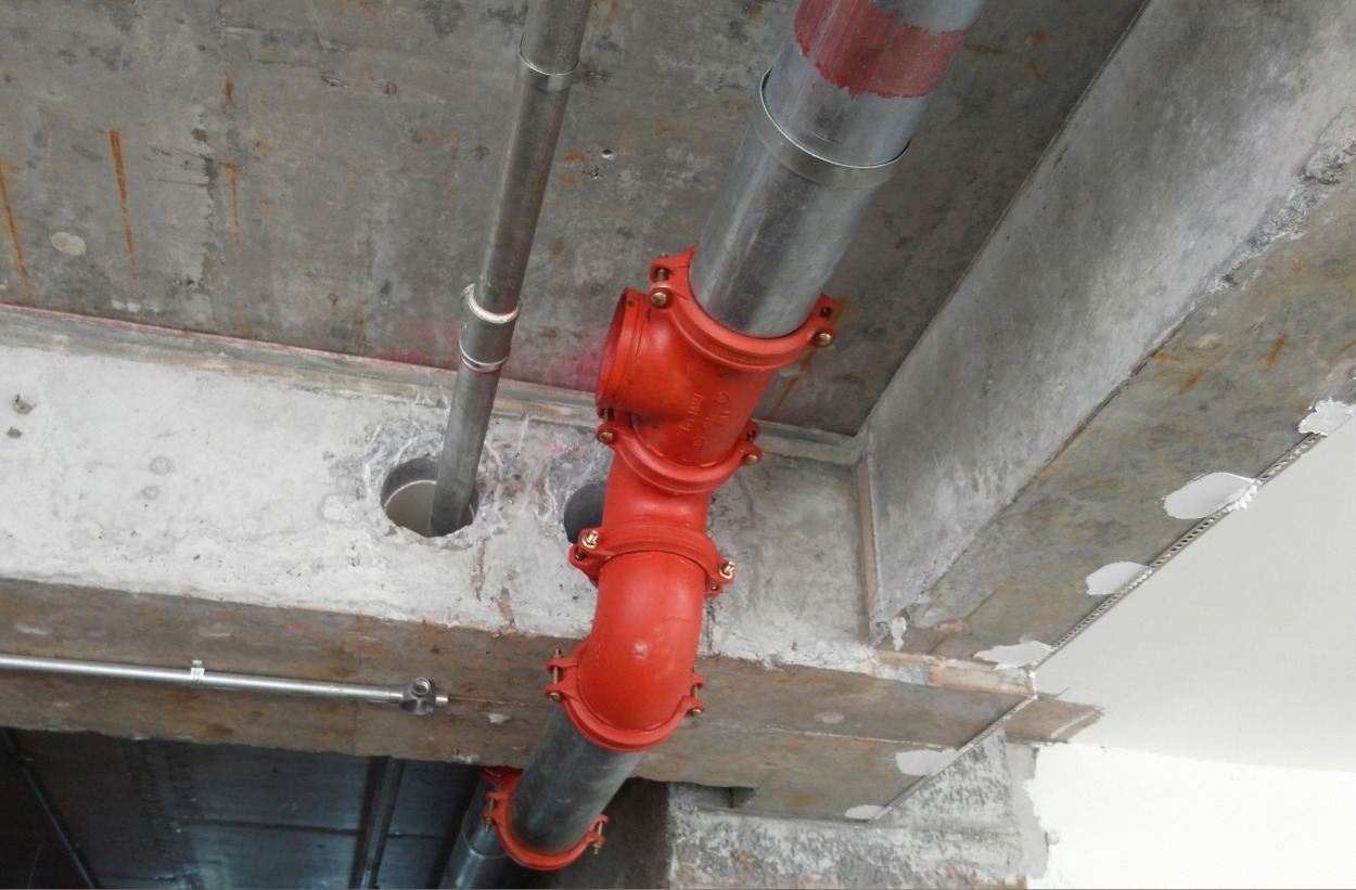 Industrial metal pipes with bright orange joints installed along a concrete ceiling.
