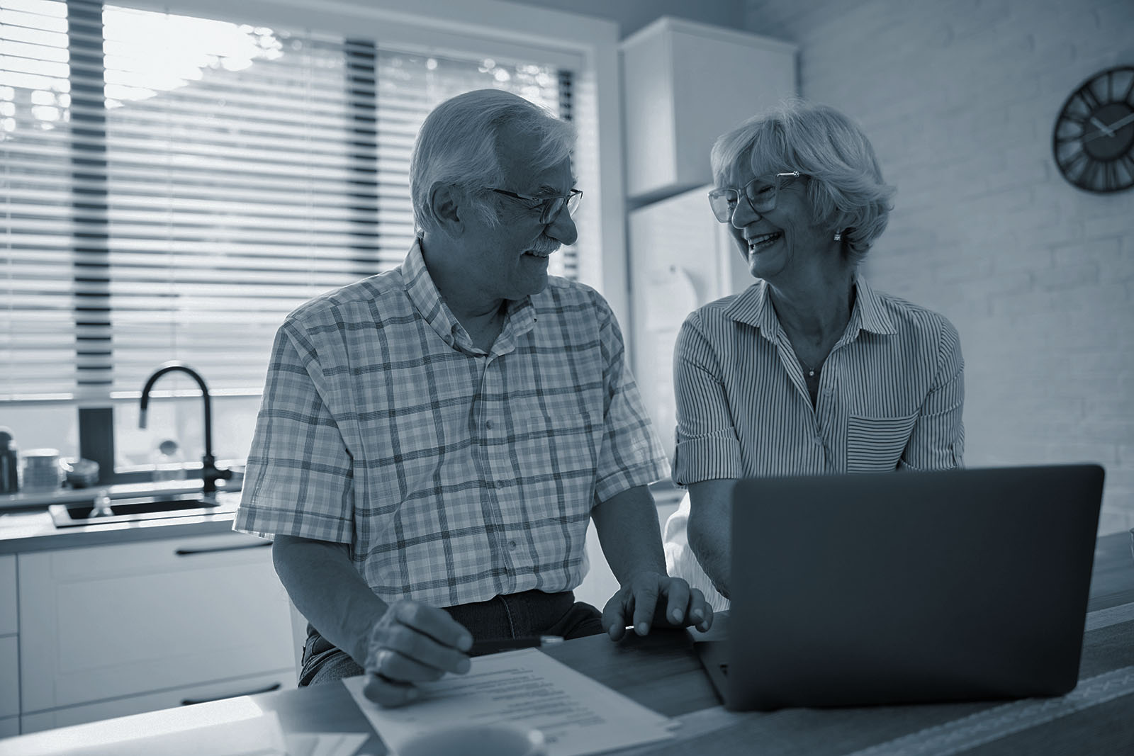 Senior couple reviewing their investment portfolio on a laptop at their kitchen counter, shown in Ignite's blue duotone style