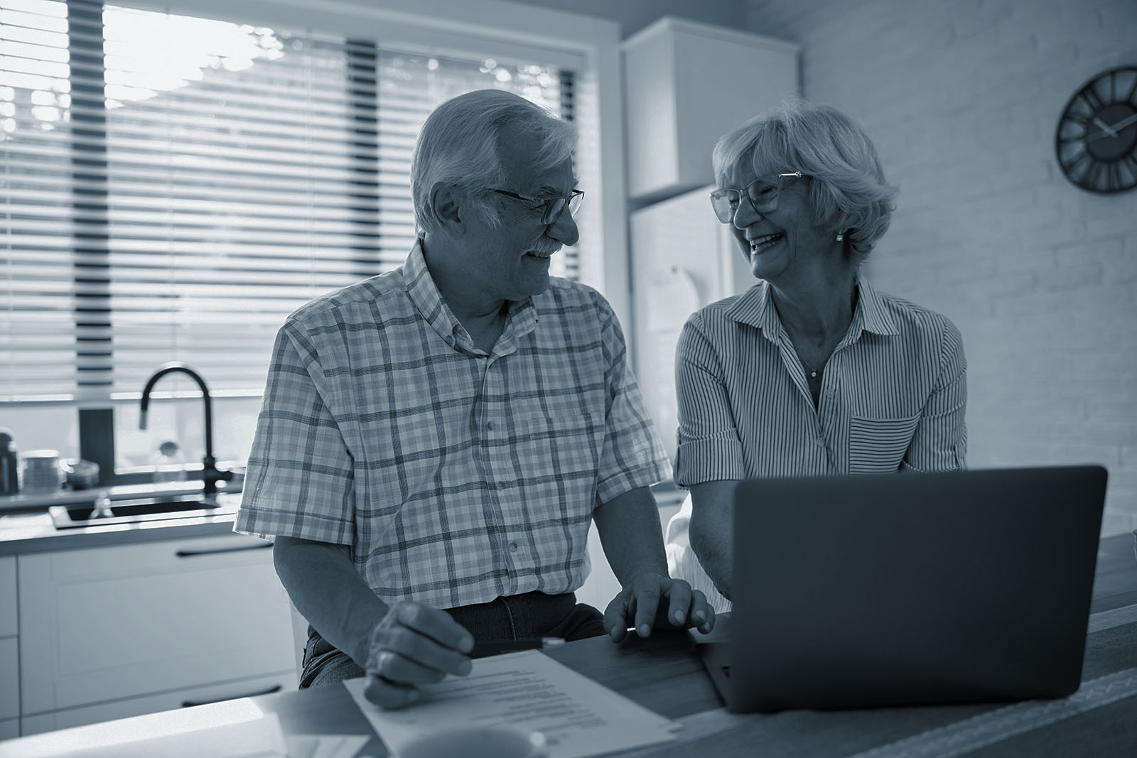 A married couple reviewing their retirement finances together at a kitchen counter with a laptop and paperwork
