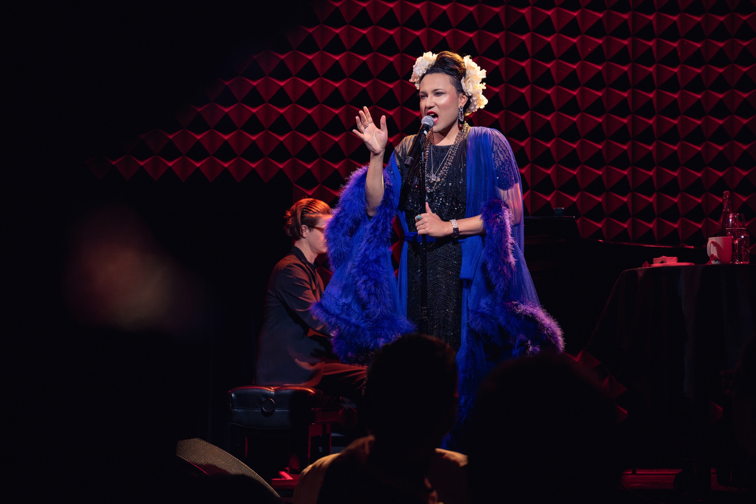 Mama Alto, in a blue feathery gown, performs in an atmospheric jazz club setting