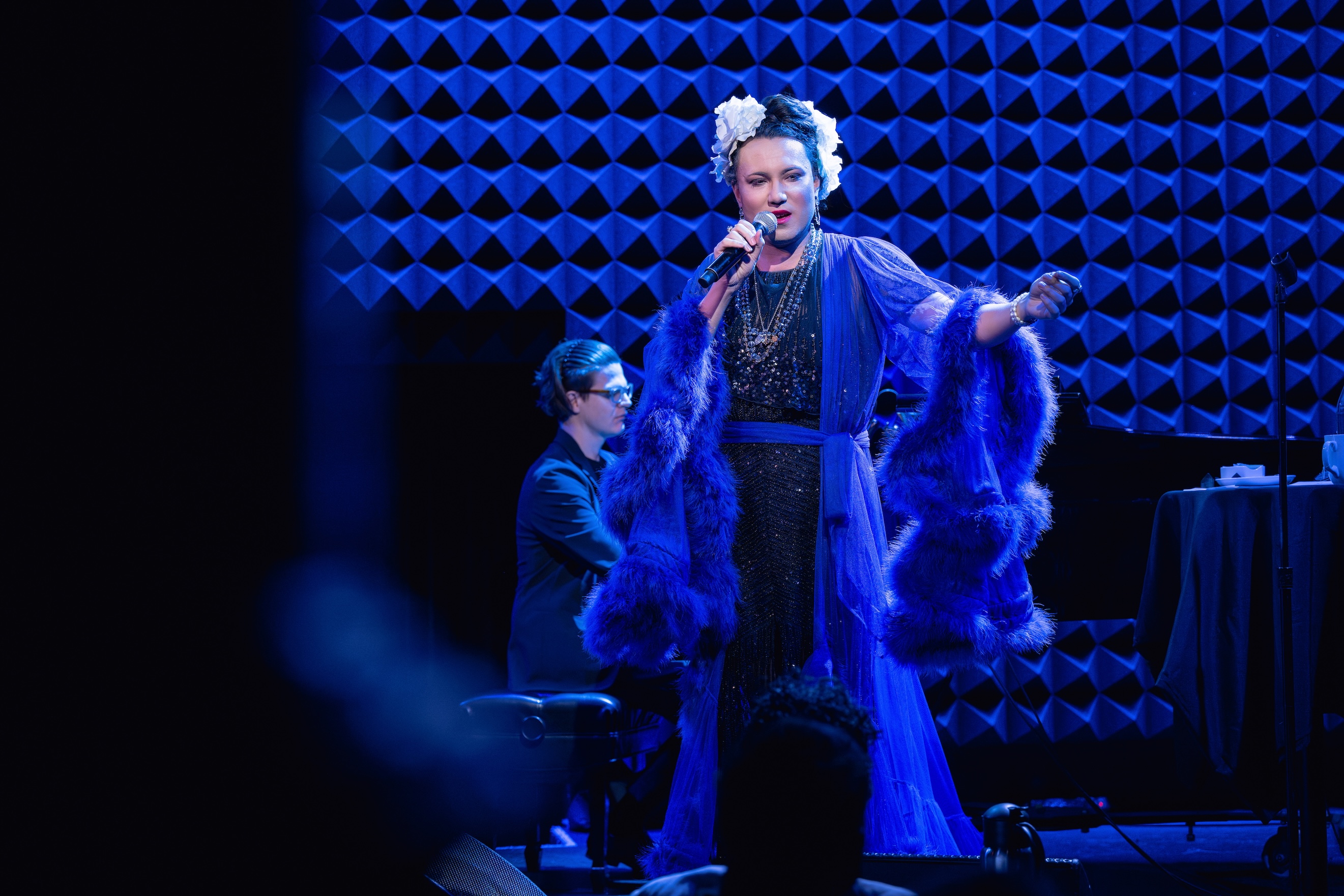 Mama Alto, in a blue feathery gown, performs in an atmospheric jazz club setting