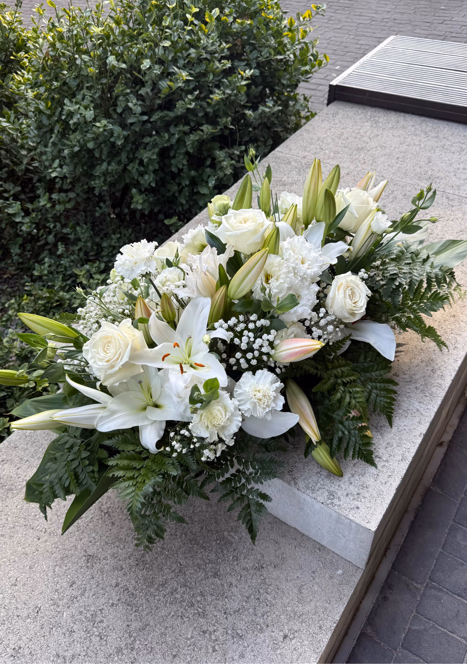 Leżąca kompozycja pogrzebowa z białych lilii, róż, goździków i zieleni dekoracyjnej