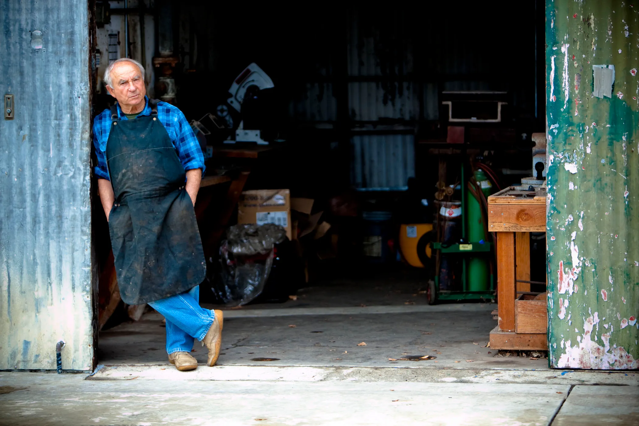 Yvon Chiounard leaning against a sliding tin shed door in a metalworkers apron