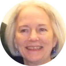Smiling older woman with light blonde hair and blue top against a light background.